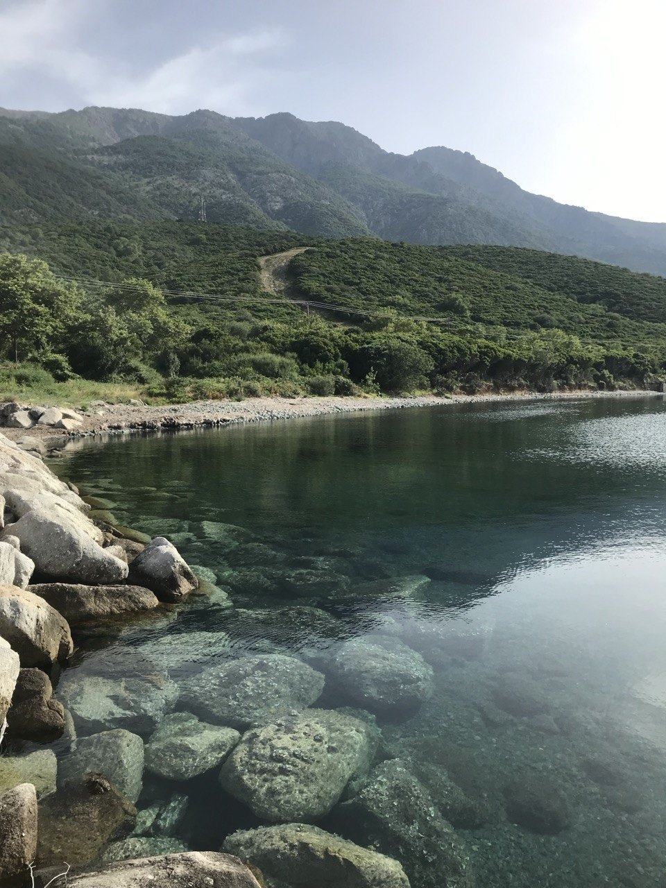 Clear water over smooth stones in a cove, with green slopes and the mountain behind