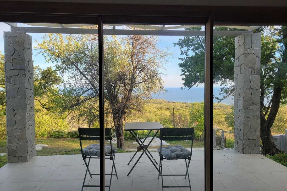 Covered terrace with two chairs looking out over trees to the sea